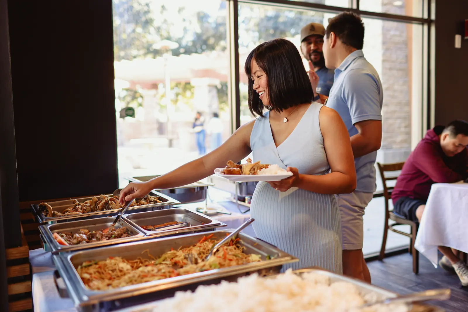 A smiling mom-to-be fills her plate at the buffet at Max's Chula Vista, beside trays of pancit, lumpia and fried chicken