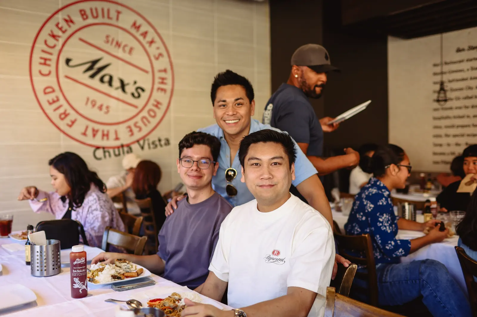 Three guests smile at their table in front of the Max's Since 1945 wall sign at Max's Chula Vista