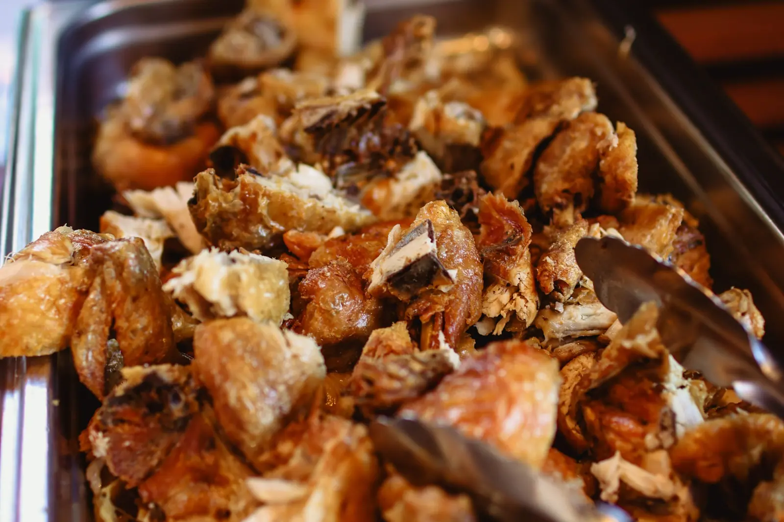 A chafing tray of Max's Fried Chicken, chopped and ready to serve, with tongs