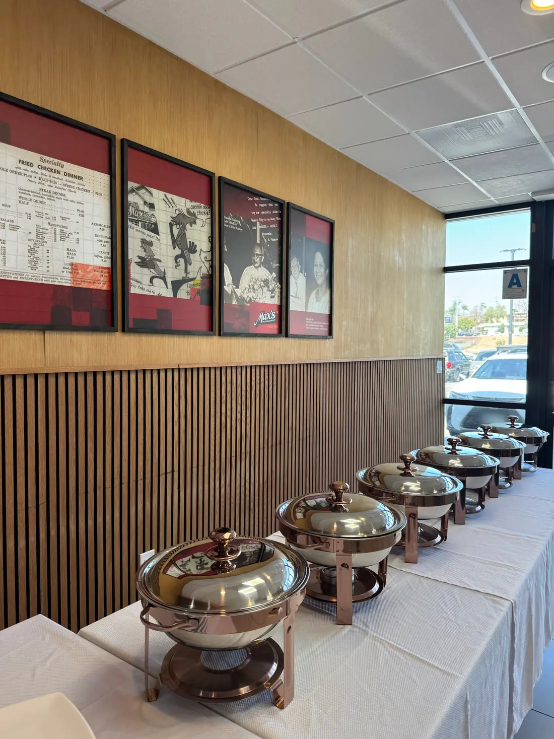 A row of copper-tone chafing dishes on a white buffet table along the wood-slat wall at Max's National City