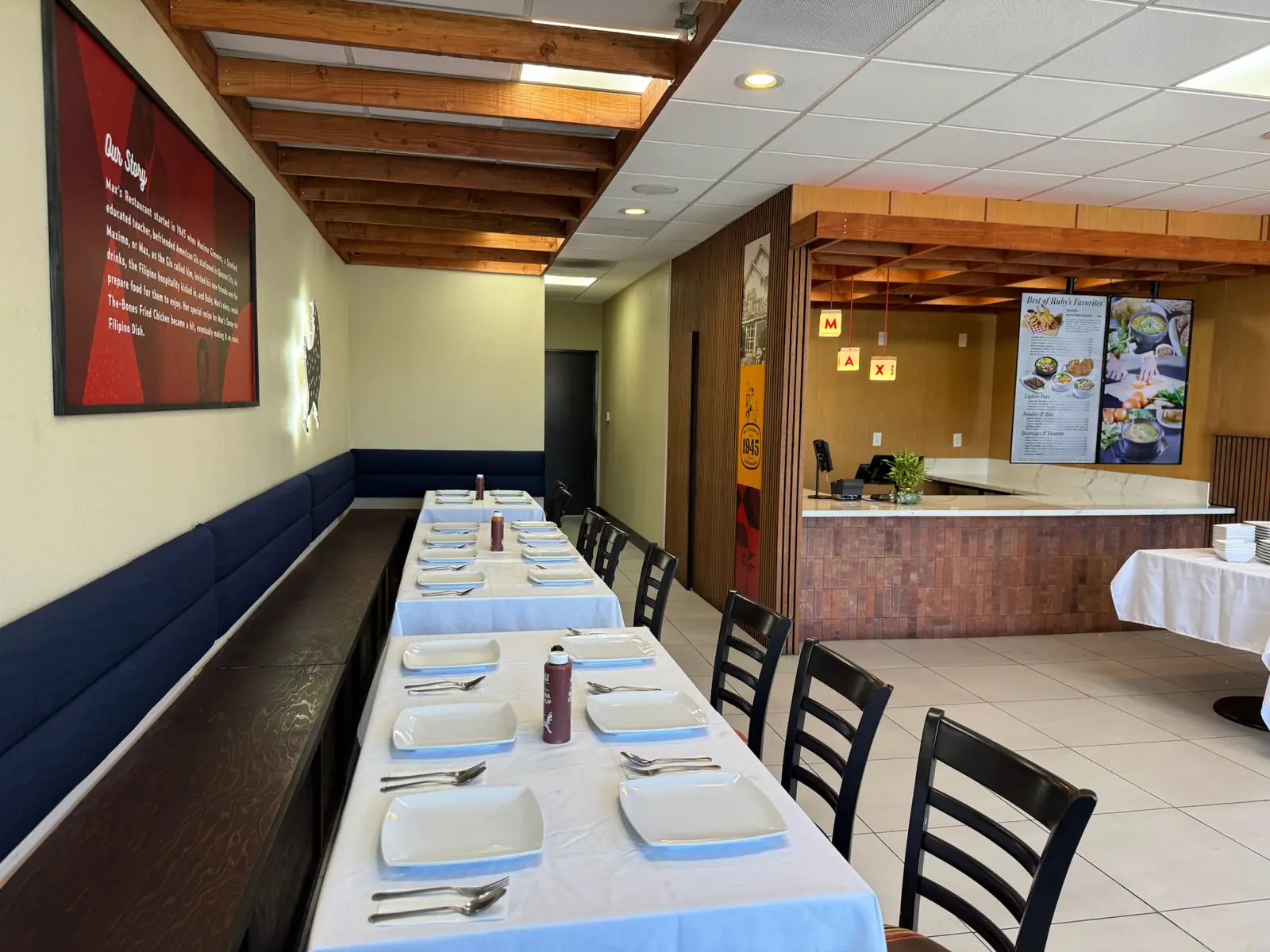 Long tables with white linens and place settings along a navy banquette beneath the Our Story wall at Max's National City