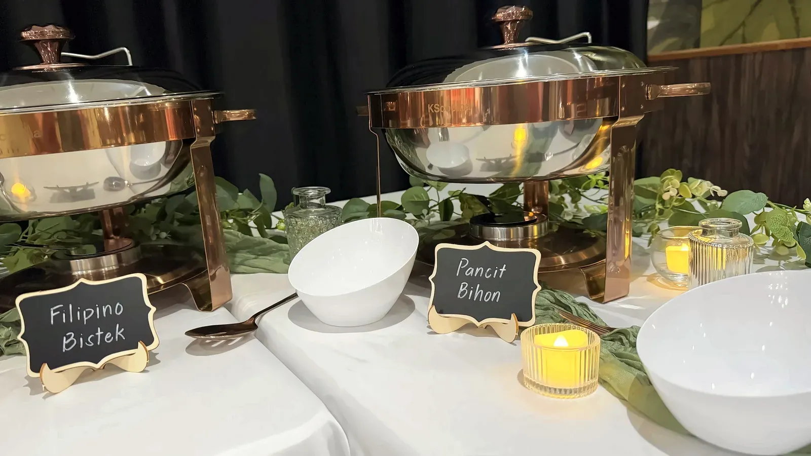 Chafing dishes labeled Filipino Bistek and Pancit Bihon with serving bowls and candles on the buffet at Max's San Diego