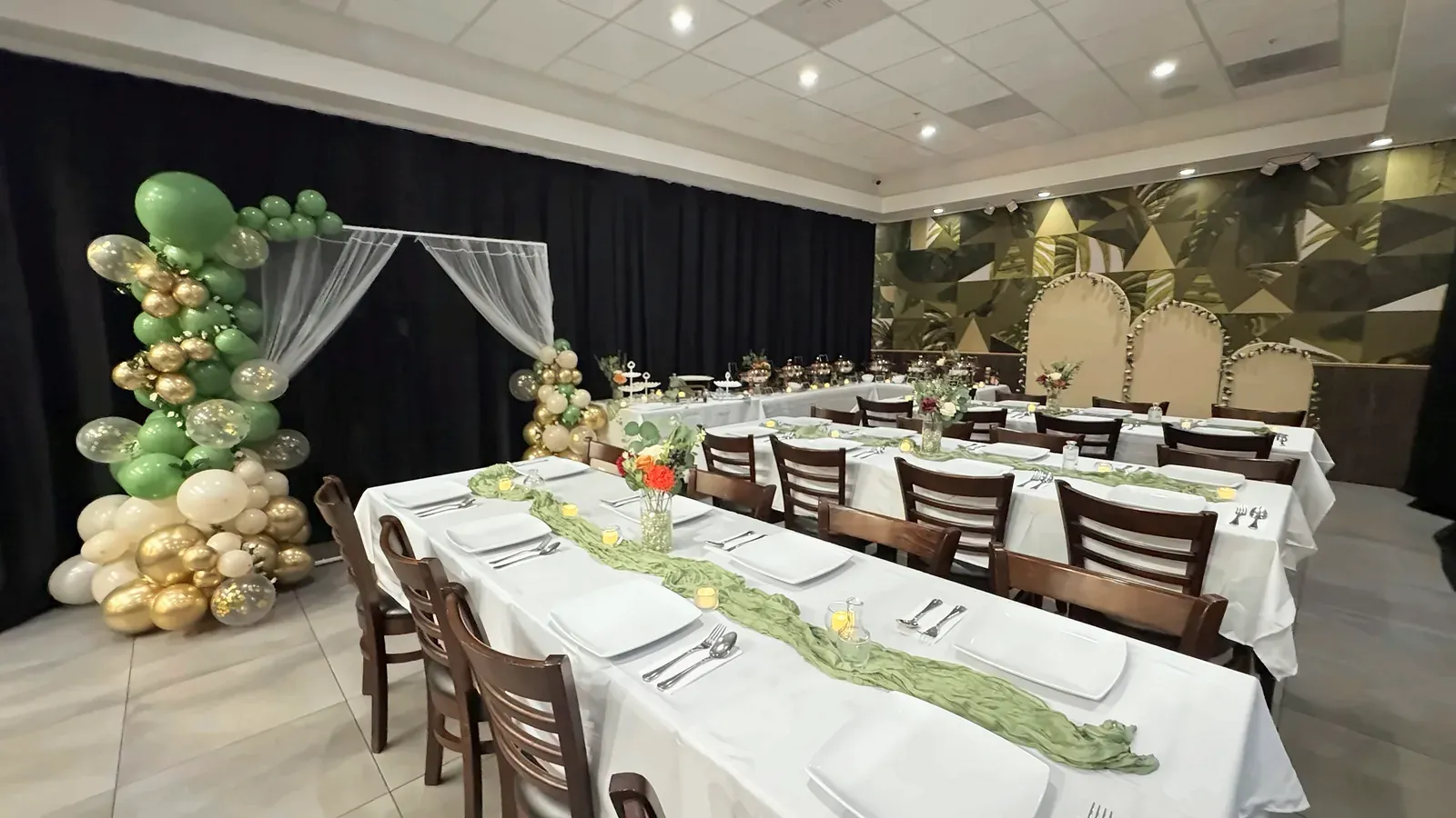 A balloon arch, long tables with green runners and a buffet line along the back wall, set for a party at Max's San Diego