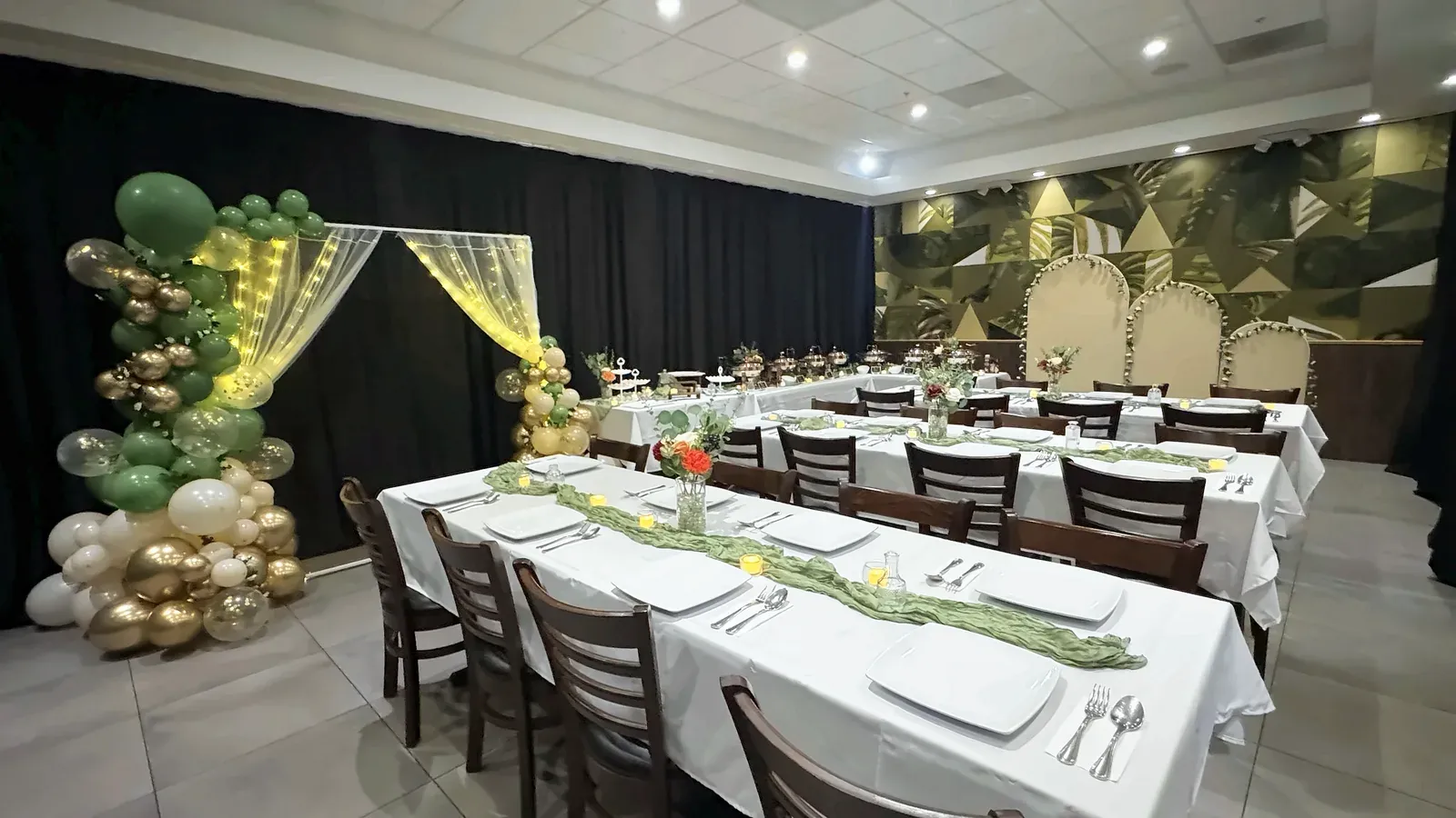 Long tables with white linens, green runners and place settings in front of the leaf mural and arched backdrop at Max's San Diego