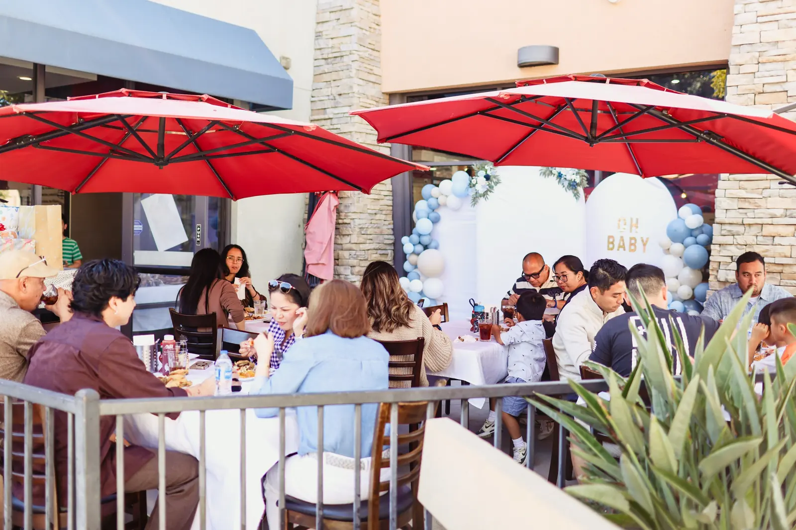 A baby shower on the Max's Chula Vista patio: guests at tables under red umbrellas, with an Oh Baby balloon arch by the door